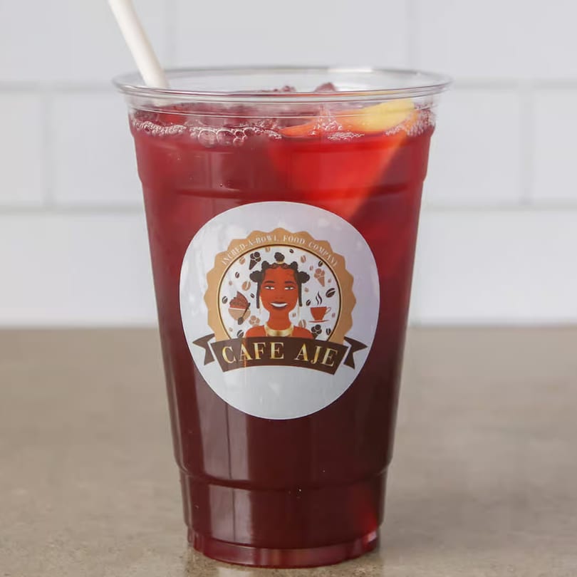 A clear plastic cup of red iced tea with a straw and a Cafe Aje logo sticker.