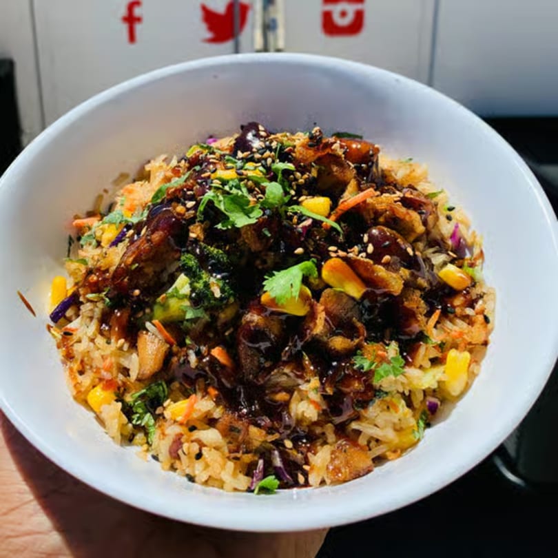 A healthy Incred-A-Bowl Food Co. bowl with rice, chicken, vegetables, and dark sauce.