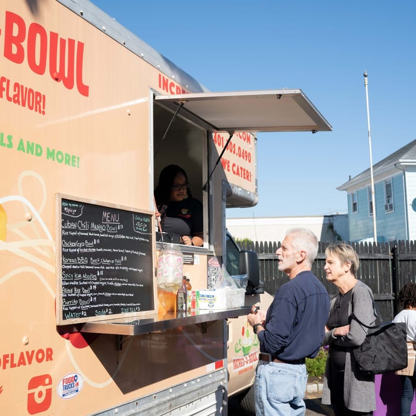 A customer orders from the Incred-A-Bowl Food Co food truck, featuring a menu of healthy bowls.