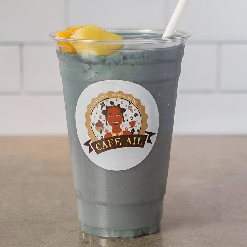 A blue smoothie with pineapple and orange slices, a white straw, and a Cafe Aje sticker.
