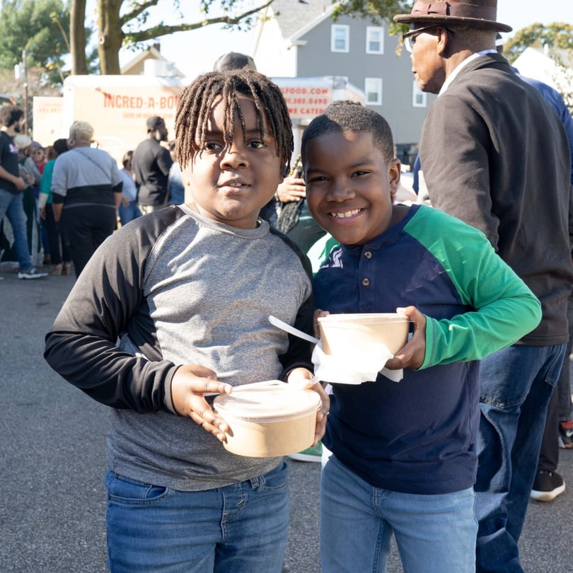 Two smiling boys holding Incred-A-Bowl Food Co. bowls at an outdoor event.