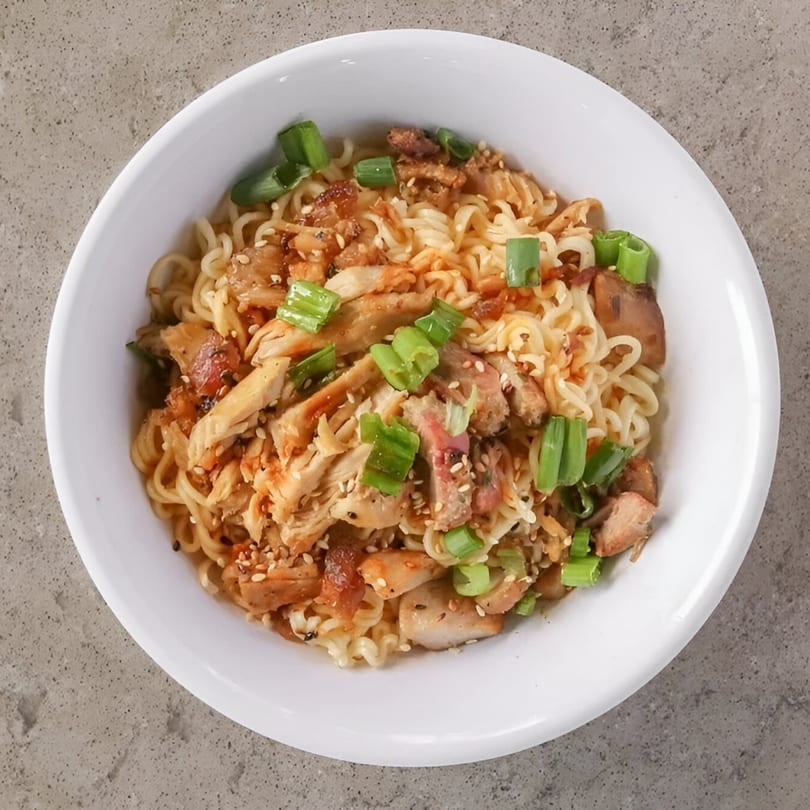 A white bowl filled with ramen noodles, chicken, sesame seeds, and chopped green onions.