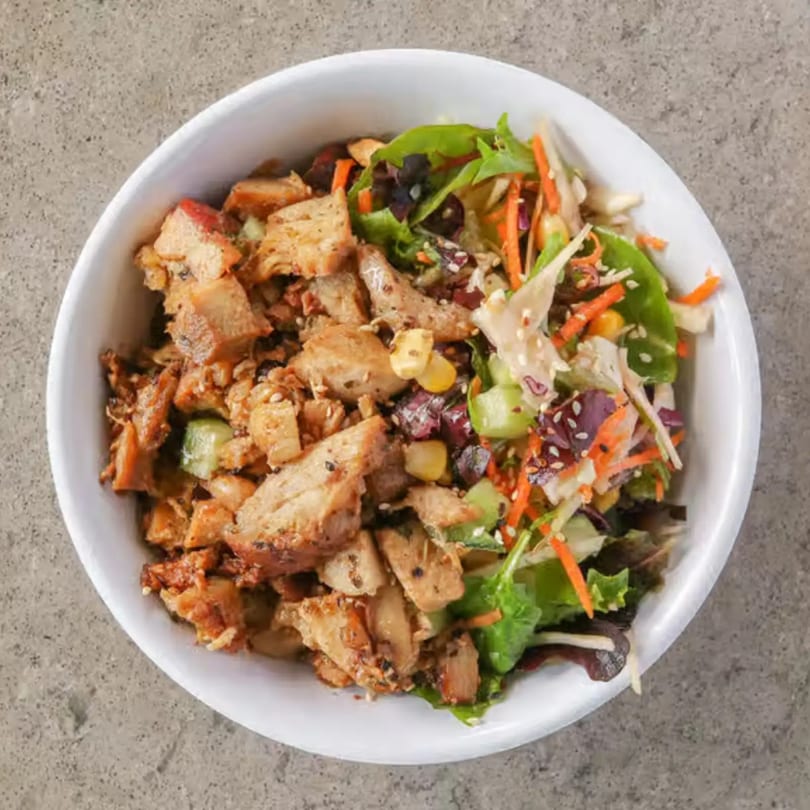 A healthy Incred-A-Bowl Food Co. bowl with grilled chicken, mixed greens, shredded carrots, and sesame seeds.