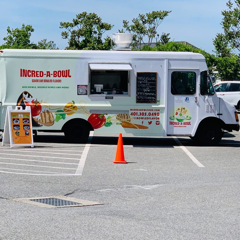 The Incred-A-Bowl food truck, with colorful food graphics, parked in a lot on a sunny day.