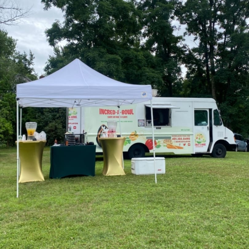 Incred-A-Bowl Food Co. food truck and white tent with tables on a grassy field.