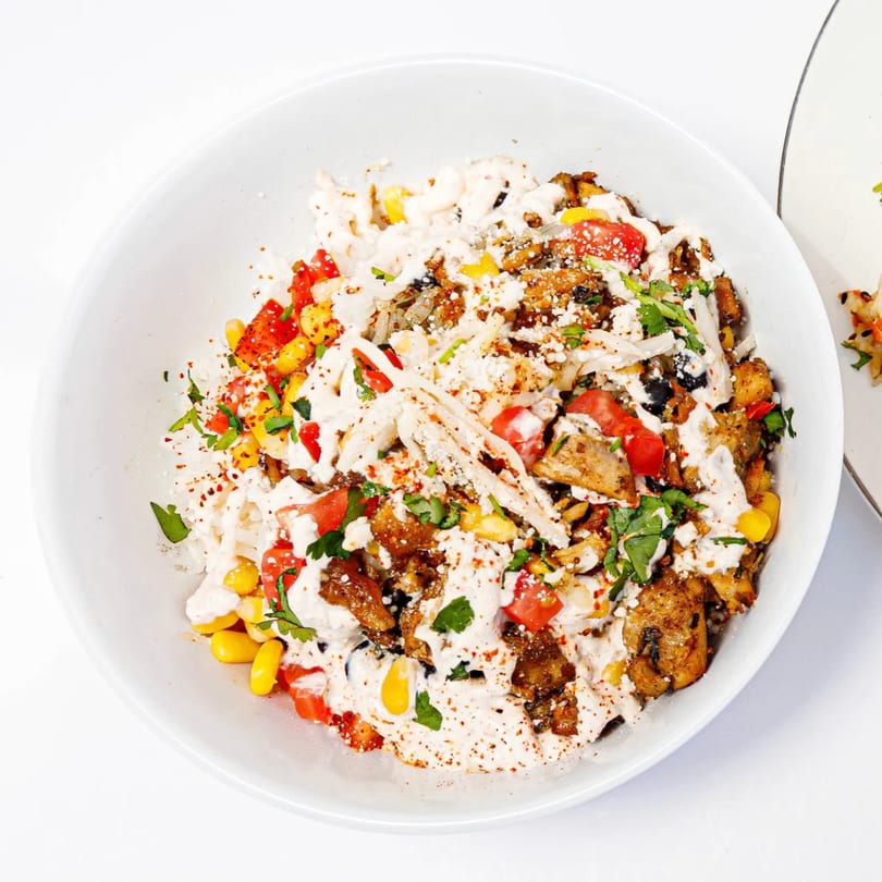 A healthy Incred-A-Bowl with chicken, corn, tomatoes, and a creamy sauce, garnished with herbs.