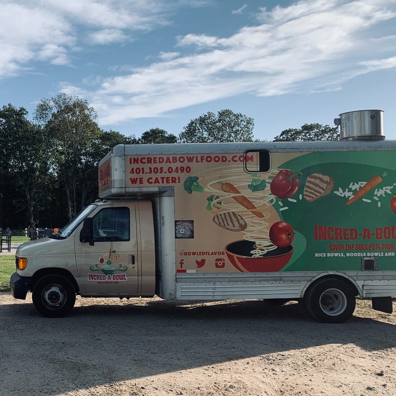 Incred-A-Bowl Food Co. food truck with colorful food graphics parked on a dirt lot.